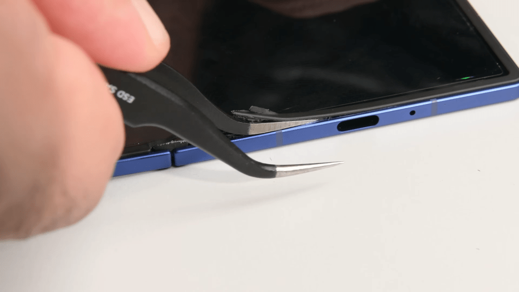 The Fold 7's bezel being chipped away at with tweezers.